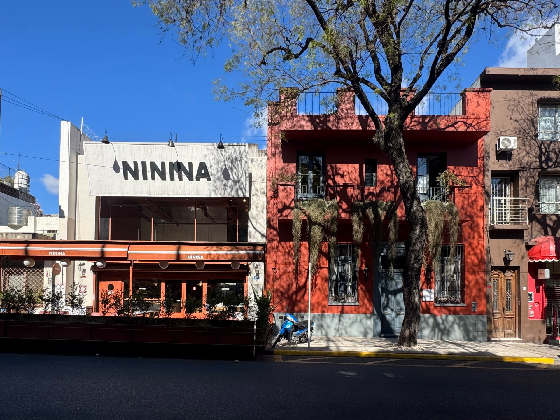 A discreet deep-red exterior wall and lush greenery blending into the quiet Palermo Soho streetscape of Buenos Aires.